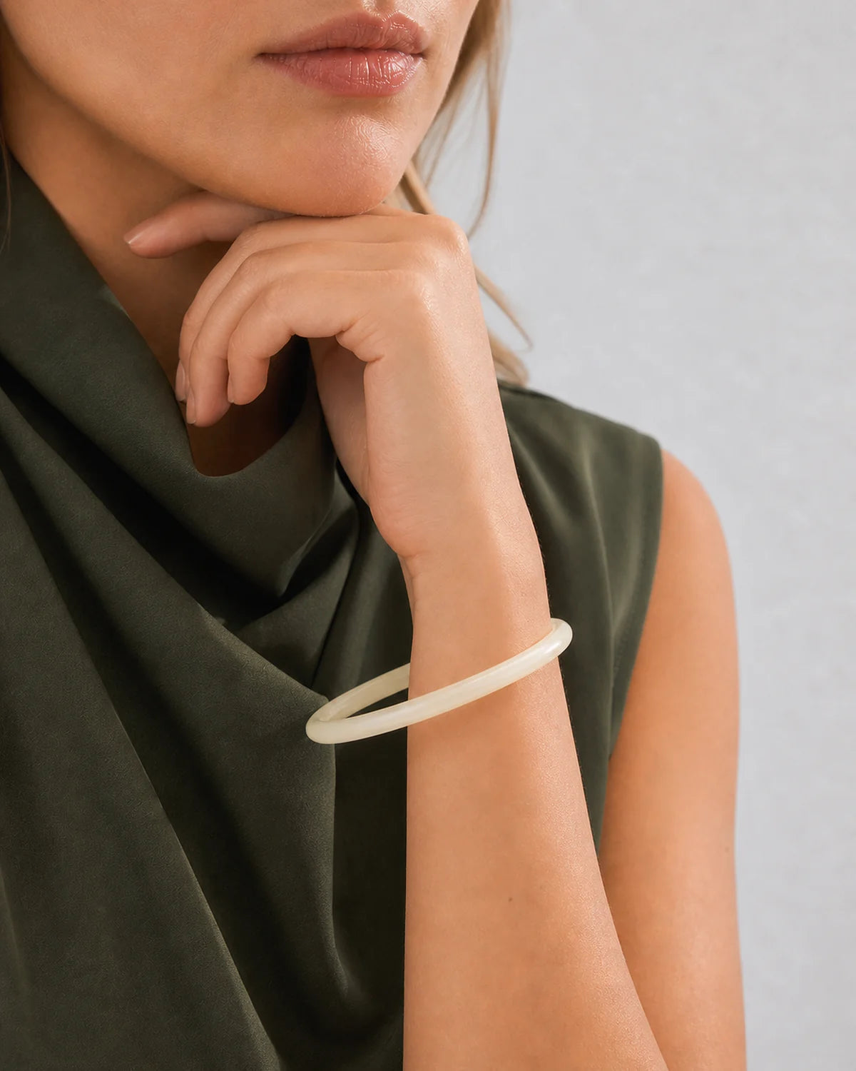 Chin-down supported-wrist detail showing the slim profile of the ivory Arden bangle