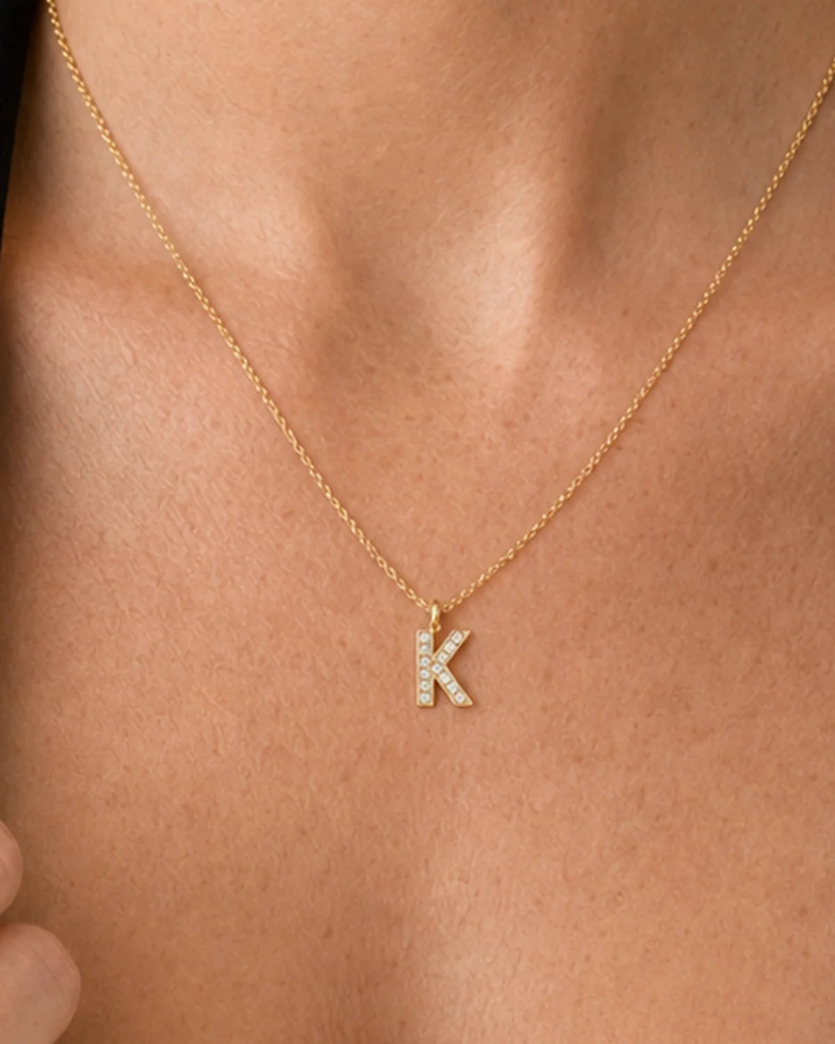 Extreme on-body macro of the Ciel clear-pavé K and fine gold chain