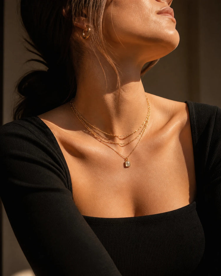 Model wearing layered gold necklaces in warm sunlight