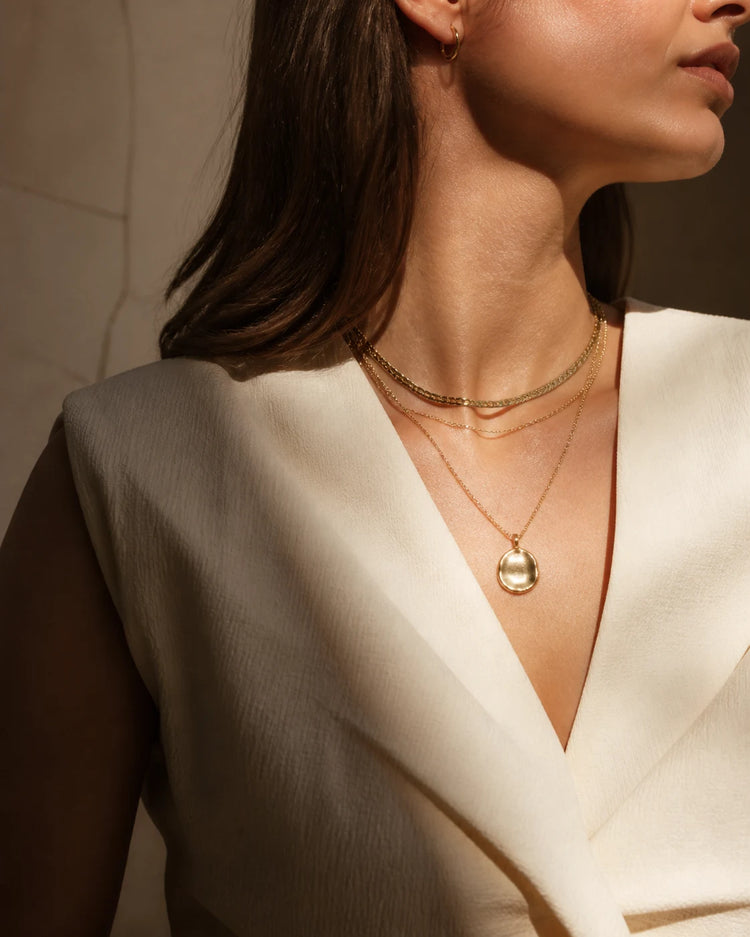 Model wearing layered gold necklaces with a medallion