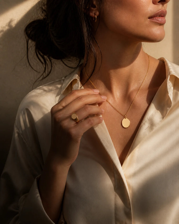 Model wearing a blank gold medallion necklace and signet ring