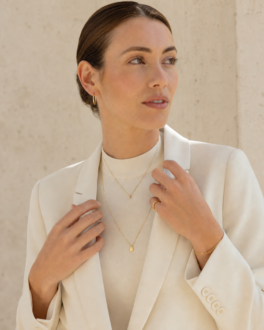 Woman in ivory tailoring wearing a considered stack of fine gold jewellery