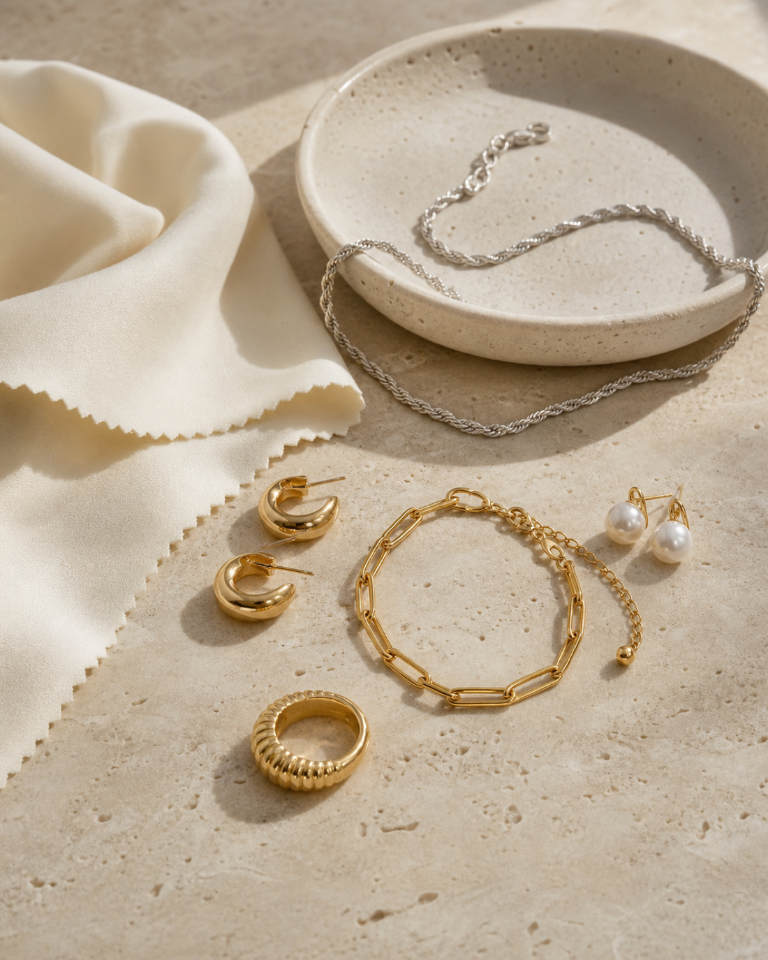 Gold, sterling silver and pearl jewellery arranged with a soft polishing cloth on travertine