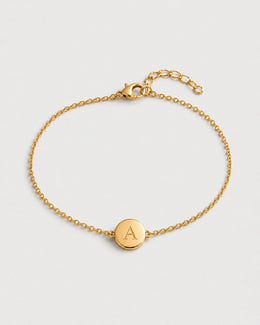 Amara gold initial A bracelet on a seamless pale dove-grey studio background