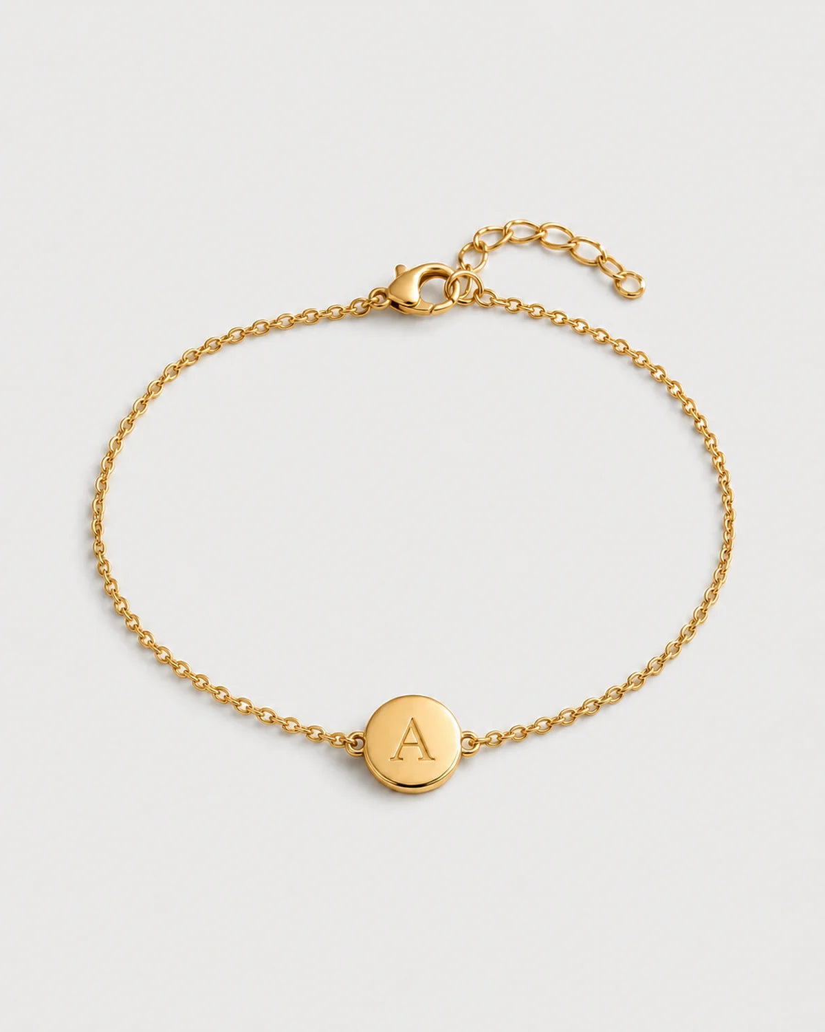 Amara gold initial A bracelet on a seamless pale dove-grey studio background