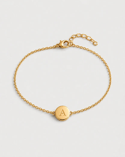 Amara gold initial A bracelet on a seamless pale dove-grey studio background