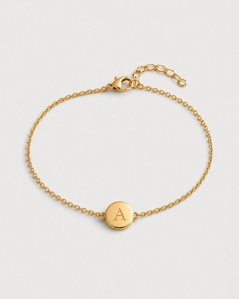 Amara gold initial A bracelet on a seamless pale dove-grey studio background