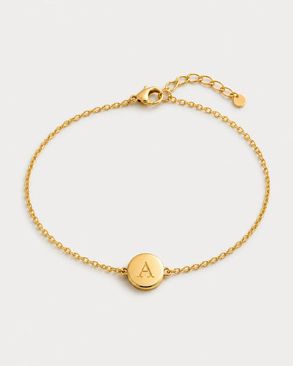 Alternate full view of the Amara gold initial A bracelet on pale dove-grey