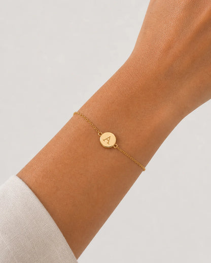 Clean wrist close-up of the Amara gold initial A bracelet on pale dove-grey