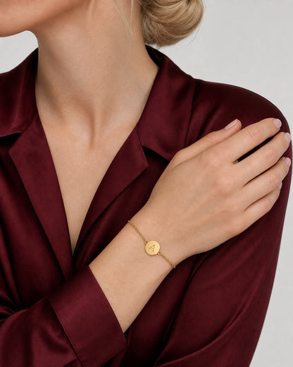 Amara gold initial bracelet worn on a diagonal wrist against a garnet silk blouse