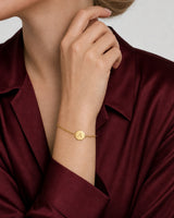 Amara gold initial bracelet worn on a lifted wrist near the lower jaw