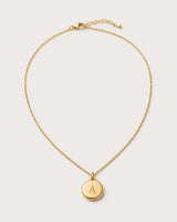 Amara gold initial A medallion necklace on a seamless pale dove-grey studio background