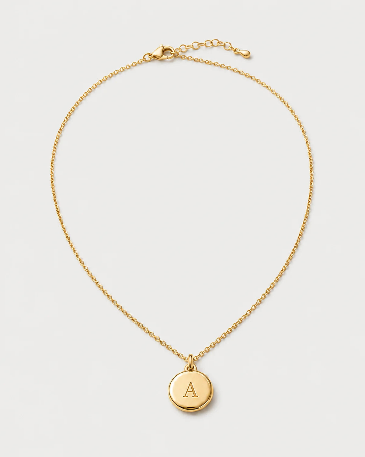 Amara gold initial A medallion necklace on a seamless pale dove-grey studio background
