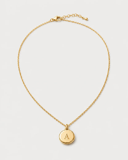Amara gold initial A medallion necklace on a seamless pale dove-grey studio background