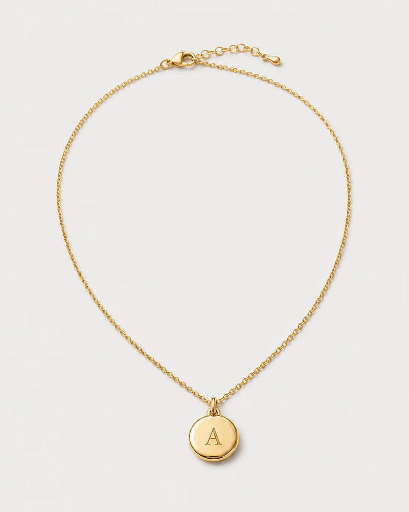 Amara gold initial A medallion necklace on a seamless pale dove-grey studio background