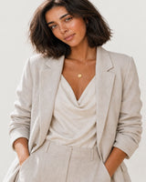 Australian model aged 25 to 28 wearing the Amara initial medallion necklace in a pale dove-grey studio