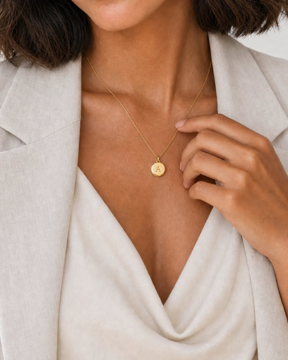 Human-scale hand and neckline detail of the Amara initial A medallion necklace