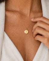 Extreme on-body macro of the Amara engraved A medallion and fine gold chain