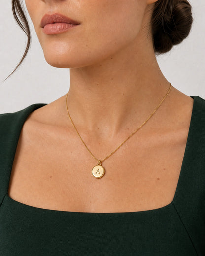 Mouth-and-chin-down portrait wearing the gold Amara initial medallion with forest green