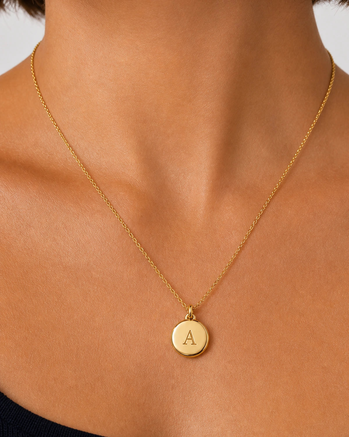 On-body macro of the Amara polished gold medallion and centered serif A