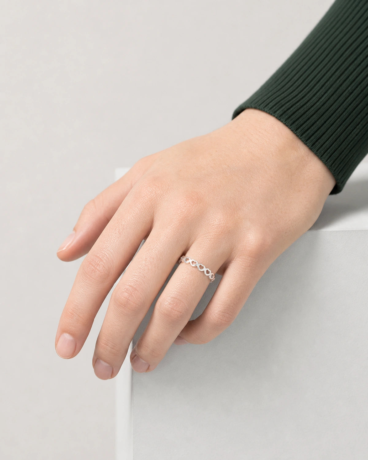 Camille wearing the silver Amoura open-heart ring with her hand resting on a grey plinth