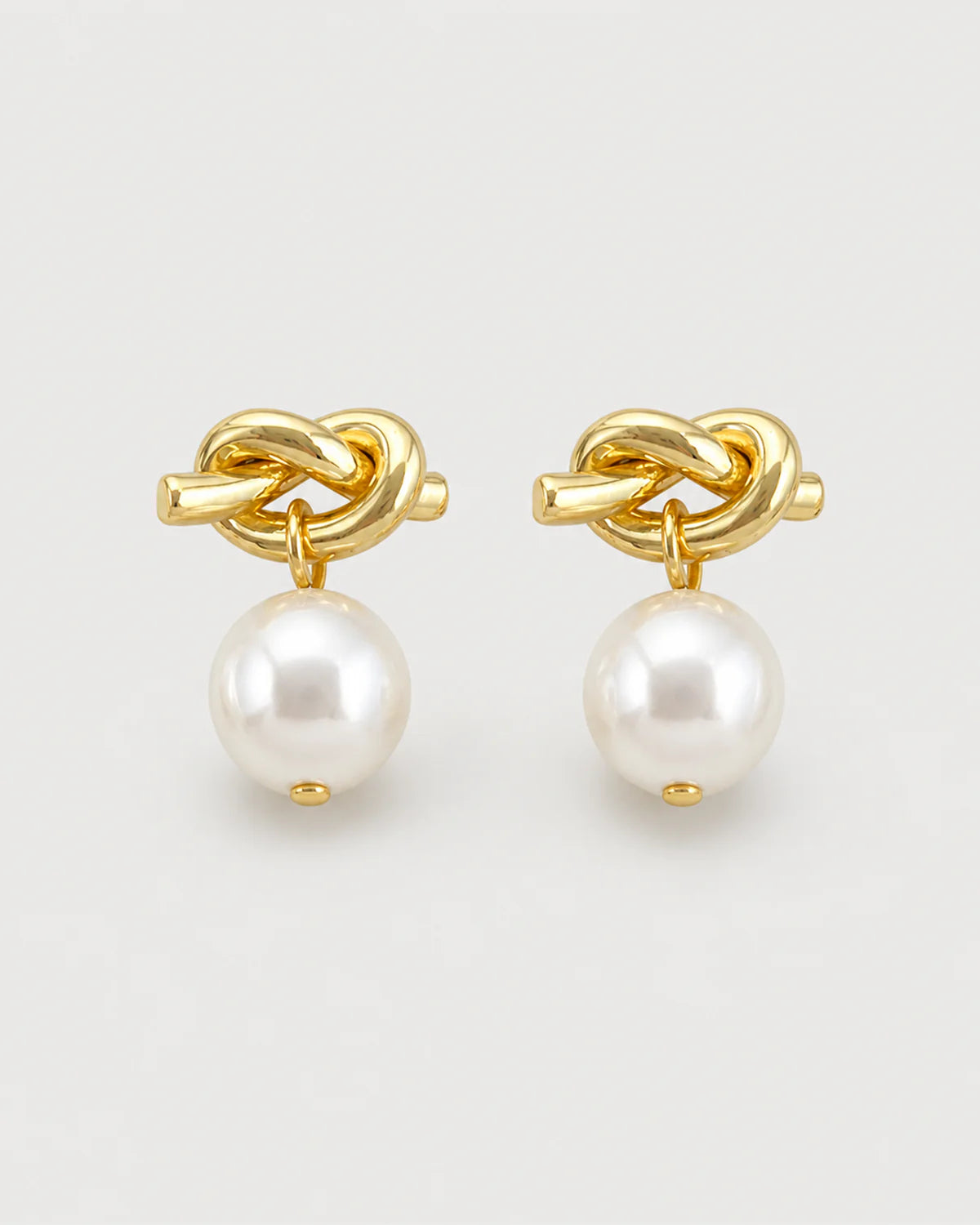 Apolline gold knot pearl drop earrings on pale dove-grey