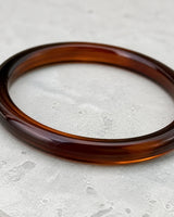 Macro of the translucent Arden espresso resin bangle on cool limestone