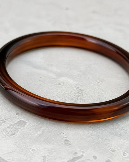 Macro of the translucent Arden espresso resin bangle on cool limestone