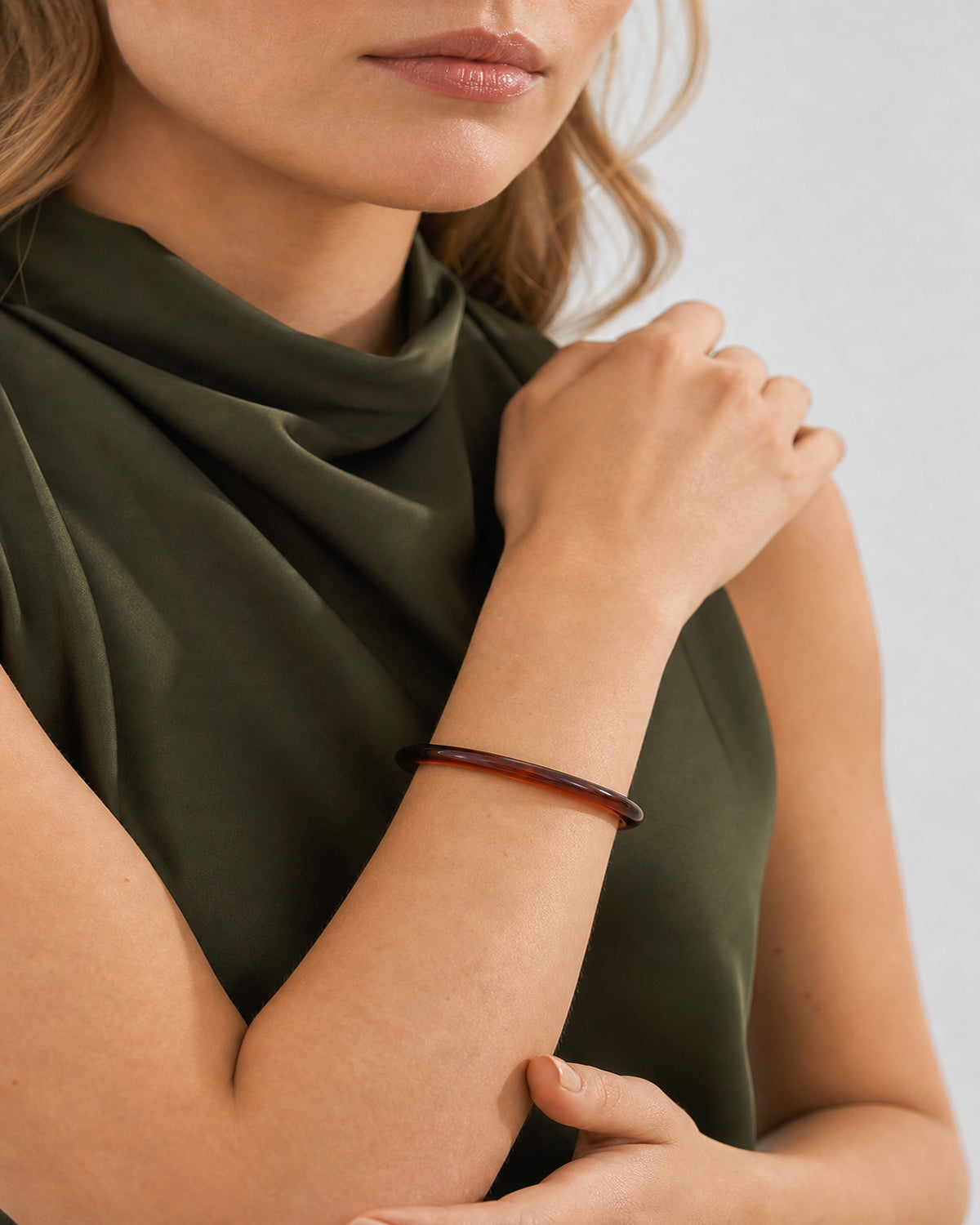 Mouth-down crossed-wrist view of Lucy wearing the espresso Arden Slim Resin Bangle