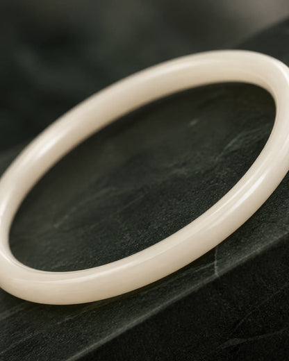 Macro of the polished Arden ivory resin bangle on deep green stone