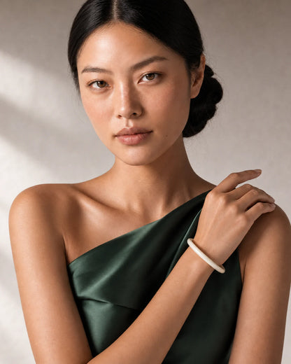 Model in forest-green satin wearing the Arden ivory bangle with a direct gaze