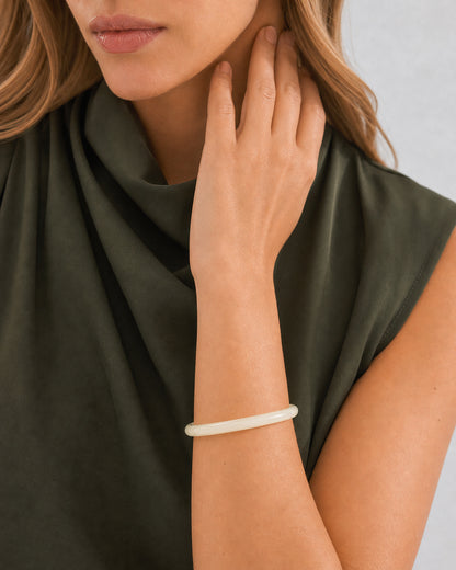 Mouth-down raised-wrist detail of the pearlescent ivory Arden bangle