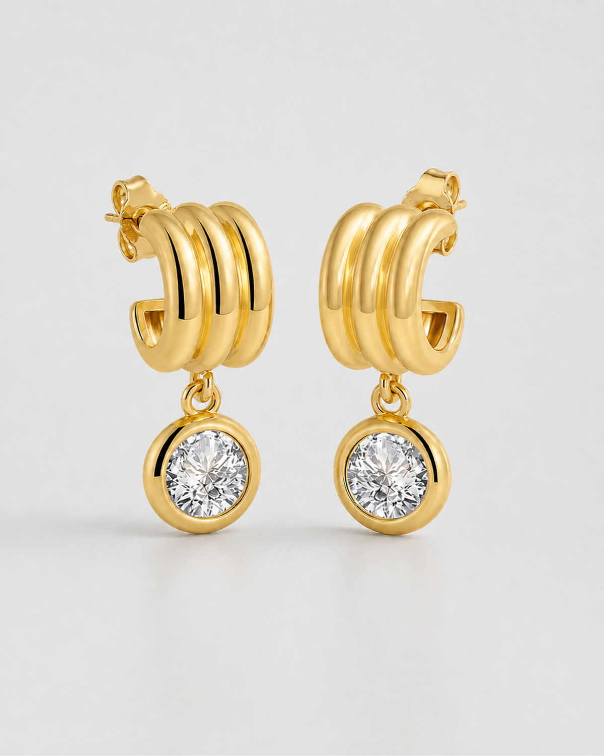 Pair of Astra gold triple-arc zircon drop earrings on seamless pale dove-grey