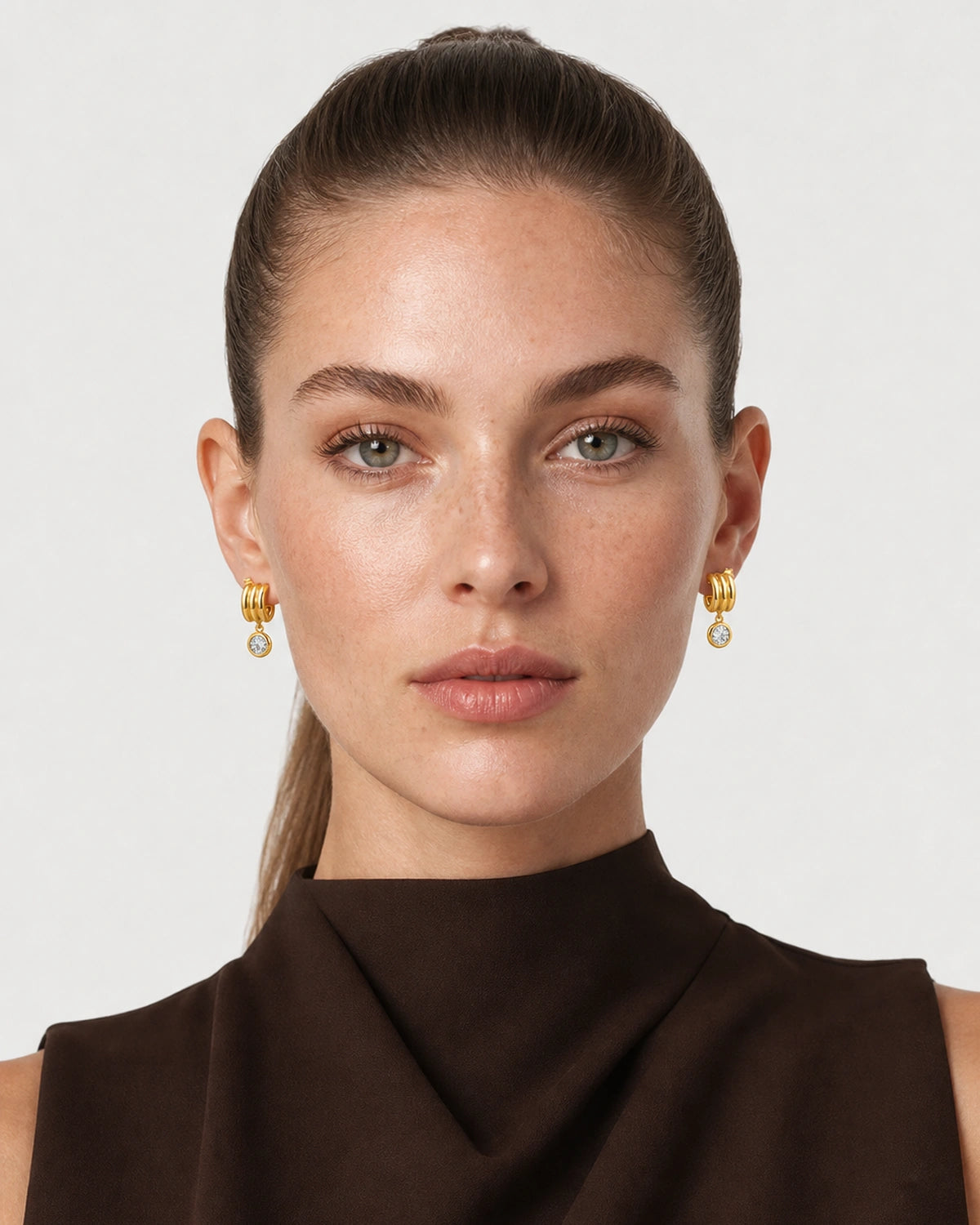 Model wearing Astra triple-arc zircon earrings in a pale dove-grey studio