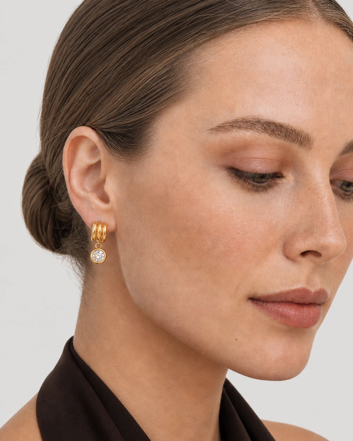 Close ear view of one Astra gold triple-arc hoop and round zircon drop