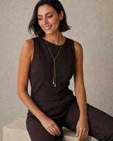 Seated model wearing the Aurelia droplet lariat in espresso tailoring with a candid smile