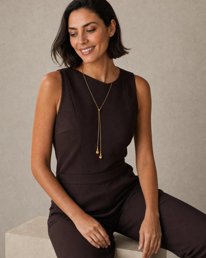 Seated model wearing the Aurelia droplet lariat in espresso tailoring with a candid smile