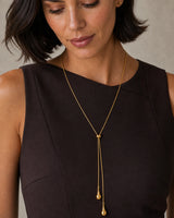 Clean close-up of the Aurelia droplet lariat worn over espresso tailoring