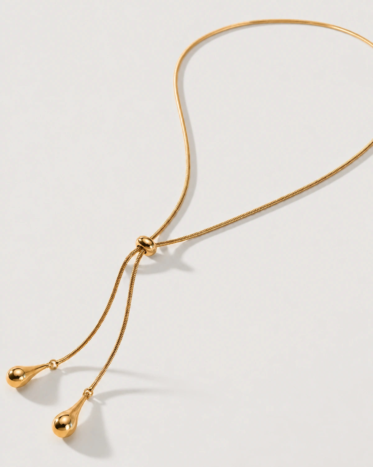 Aurelia gold droplet lariat necklace on a sculptural ivory curve