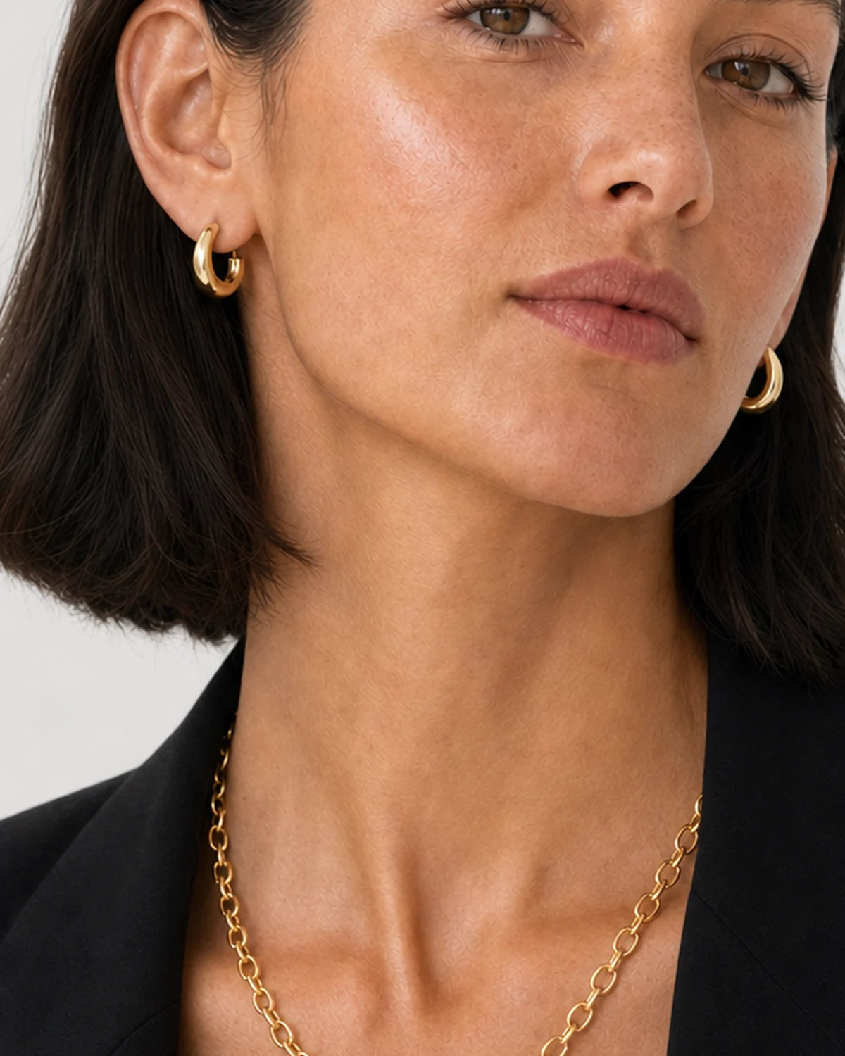 Clean close-up of the Aurelle sculpted hoops and gold oval-link necklace
