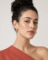 Face portrait wearing the Aurelle gold sculpted open-C hoops with terracotta crepe