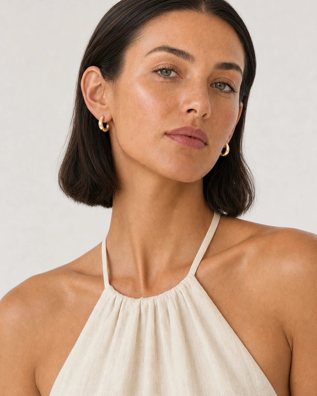 Model in an ivory Amalfi linen halter dress wearing Aurelle sculpted hoops