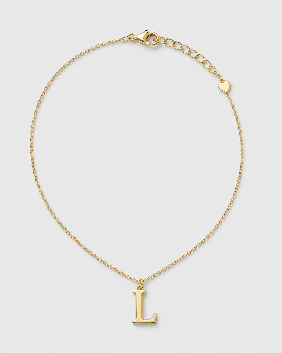 Aveline gold serif L initial necklace on a seamless pale dove-grey studio background
