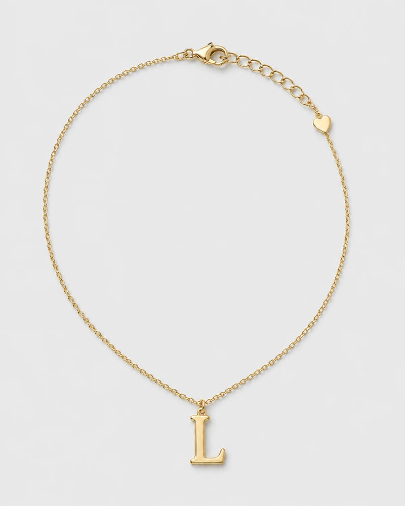 Aveline gold serif L initial necklace on a seamless pale dove-grey studio background