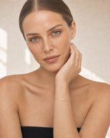 Caucasian model with wrist near her face wearing Aven gold bracelet