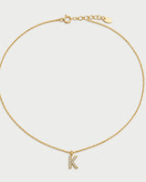 Ciel gold pavé initial K necklace on a seamless pale dove-grey studio background