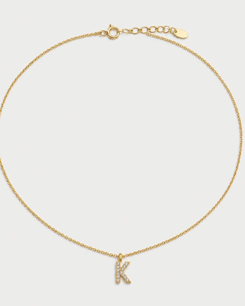 Ciel gold pavé initial K necklace on a seamless pale dove-grey studio background