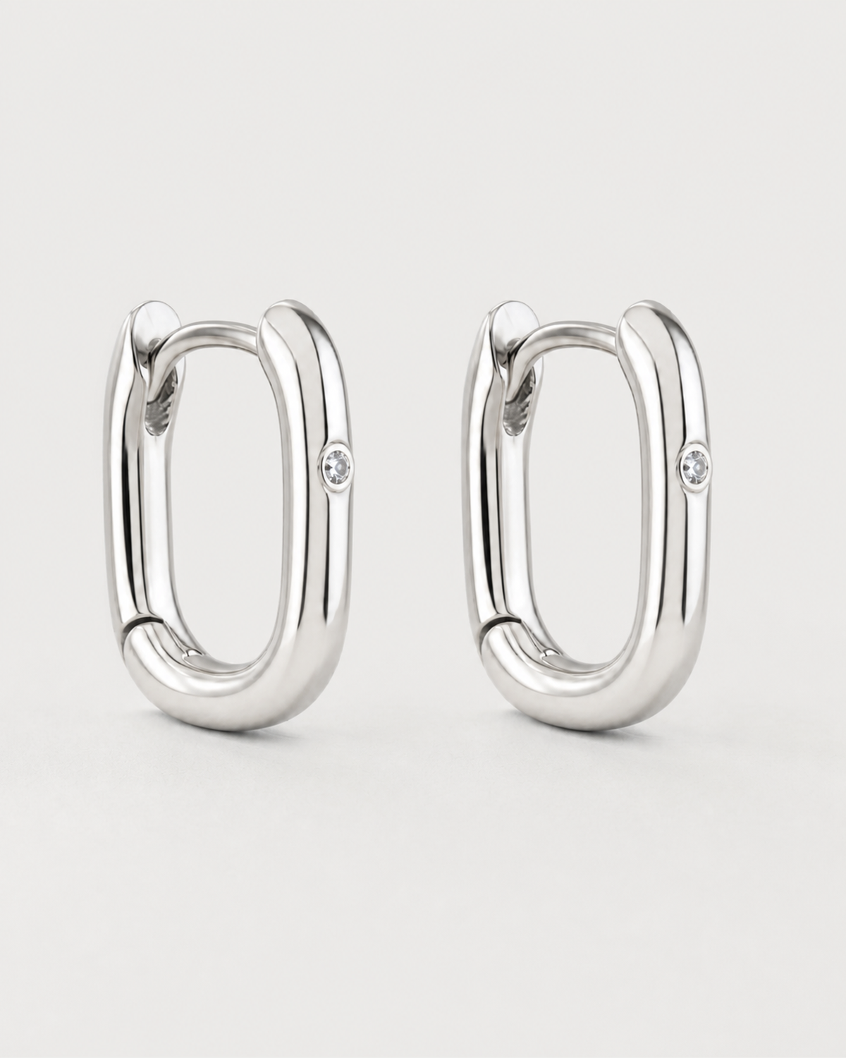 Pair of Clea sterling-silver single-crystal huggies on a seamless pale dove-grey background