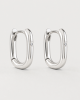 Pair of Clea sterling-silver single-crystal huggies on a seamless pale dove-grey background