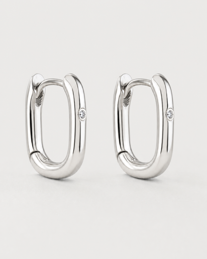 Pair of Clea sterling-silver single-crystal huggies on a seamless pale dove-grey background